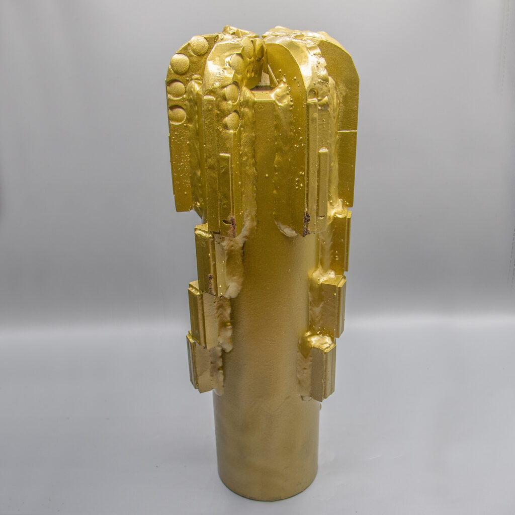 Eine hohe, zylindrische Goldskulptur mit abstrakten geometrischen Formen und strukturierten Details oben und an den Seiten.