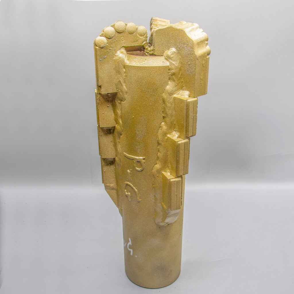 Ein goldfarbener, zylindrischer Bohrer mit gezackten Kanten und strukturierten Oberflächen auf schlichtem Hintergrund.