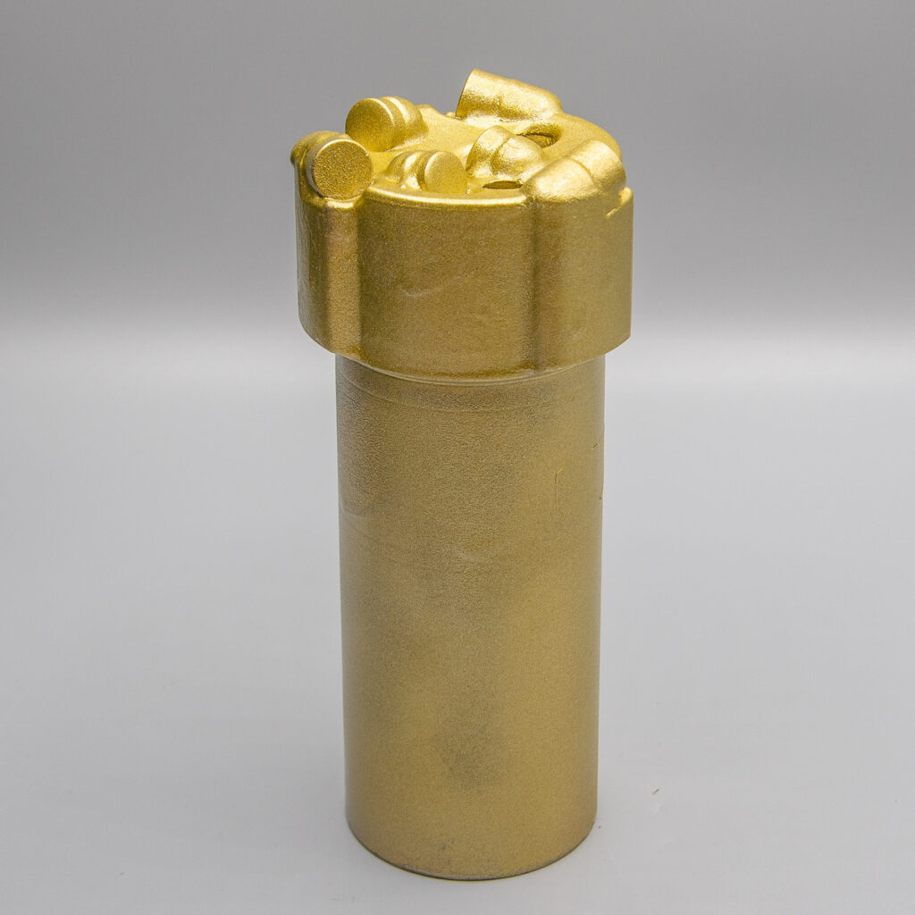 Ein goldener zylindrischer Behälter mit einem geformten, detaillierten Deckel vor einem schlichten grauen Hintergrund.